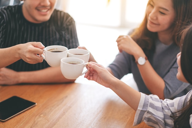 Close-up beeld van drie Aziatische mensen genoten van drinken en rammelende koffiekopjes op houten tafel in café