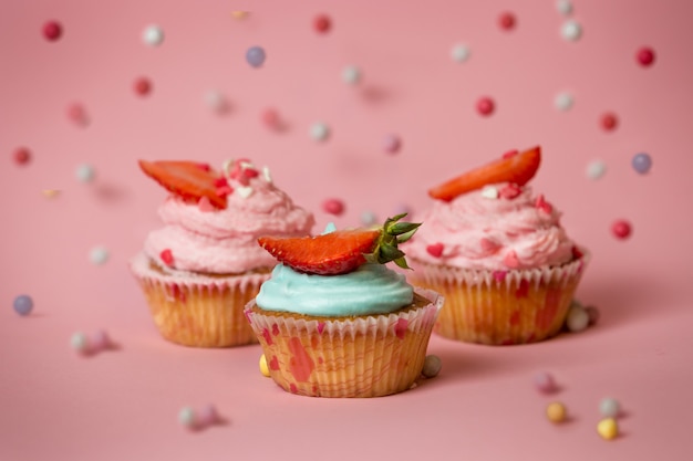 Close-up beeld van drie kleurrijke cupcakes met aardbeien op roze oppervlak met vallende snoepjes