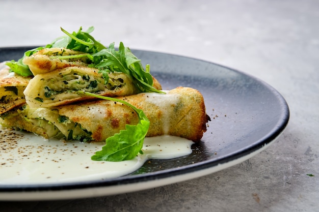 Close-up beeld van dunne crêpe gevuld met kaas, rucola en spinazie op een bord met romige saus