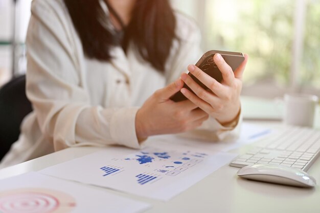 Close-up beeld van een Aziatische zakenvrouw die haar smartphone gebruikt bij haar bureau-sms-bericht