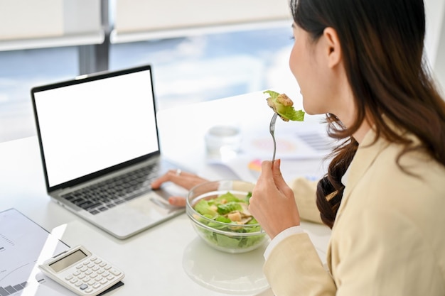 Close-up beeld van een drukke Aziatische zakenvrouw die aan het lunchen is terwijl ze op kantoor werkt