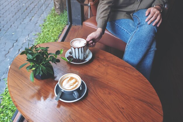 Close-up beeld van een hand met een kop warme chocolademelk met een ander kopje koffie op houten tafel in café