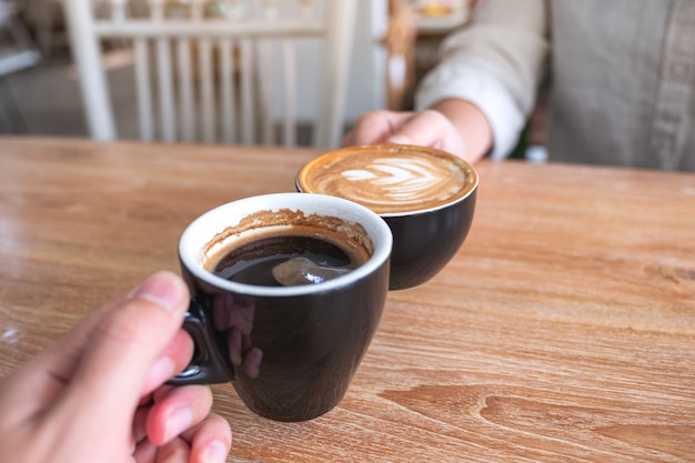 Close-up beeld van een man en een vrouw rammelende twee koffiemokken op houten tafel in café