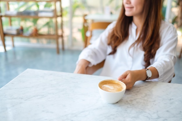 Close-up beeld van een mooie Aziatische vrouw die een kop warme koffie vasthoudt terwijl ze in café zit