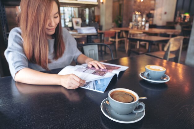 Close-up beeld van een mooie Aziatische vrouw lezing tijdschrift met koffiekopje op tafel in moderne café