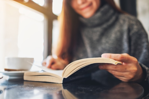 Close-up beeld van een mooie vrouw die een boek vasthoudt en leest met een koffiekopje op tafel