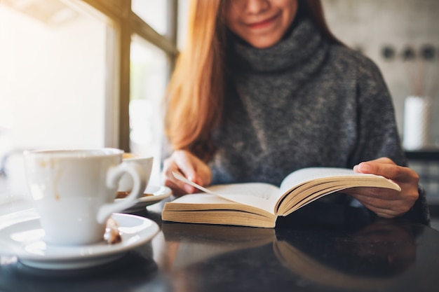 Close-up beeld van een mooie vrouw die een boek vasthoudt en leest met een koffiekopje op tafel