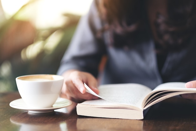 Close-up beeld van een vrouw die een boek vasthoudt en leest met een koffiekopje op houten tafel