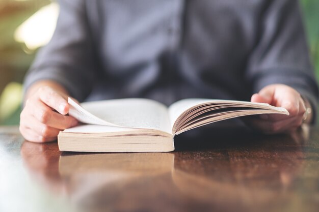 Foto close-up beeld van een vrouw die een vintage roman boek op houten tafel vasthoudt en leest