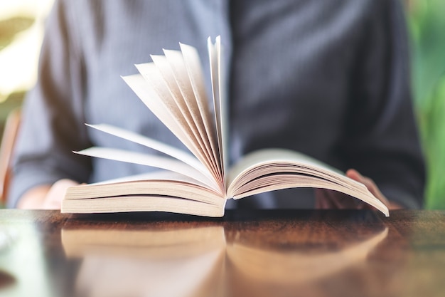 Close-up beeld van een vrouw die een vintage roman boek op houten tafel vasthoudt en leest