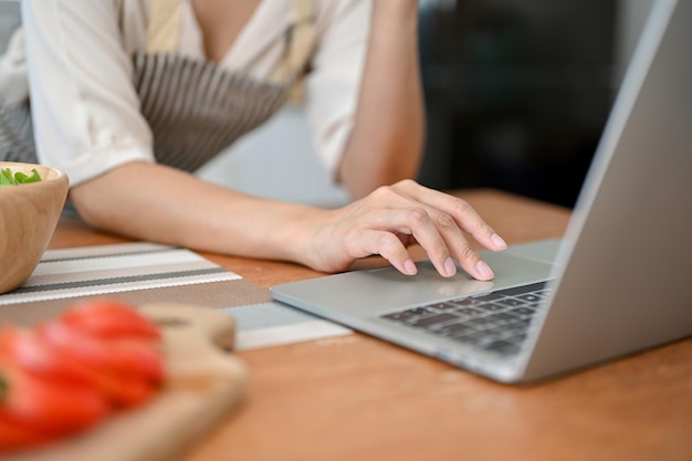 Close-up beeld van een vrouw die laptop gebruikt om voedselrecepten op internet te zoeken aan haar keukentafel