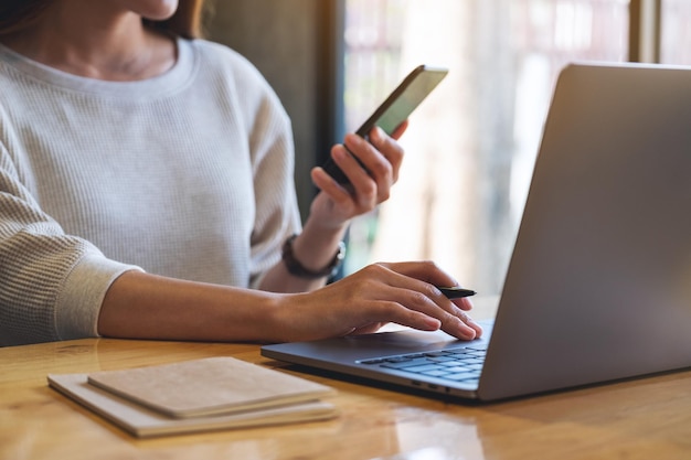 Close-up beeld van een vrouw die mobiele telefoon en laptopcomputer vasthoudt en gebruikt op kantoor