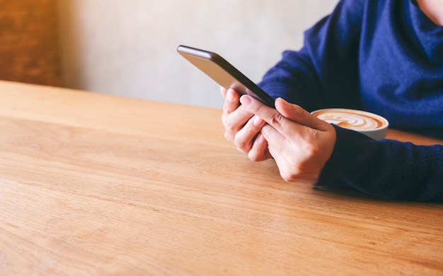 Close-up beeld van een vrouw die mobiele telefoon vasthoudt en gebruikt met koffiekopje op houten tafel