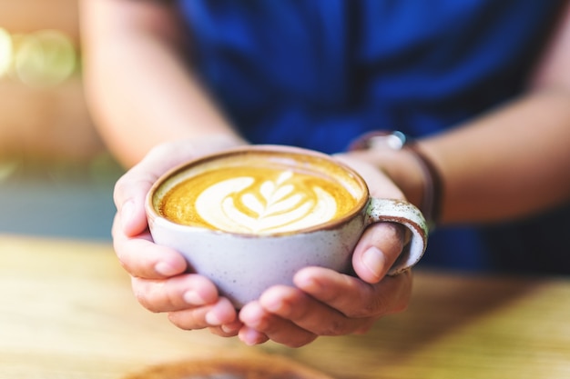 Close-up beeld van een vrouw met een kopje hete latte koffie op houten tafel