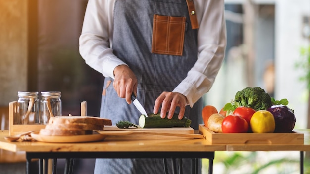 Close-up beeld van een vrouwelijke chef-kok die groenten snijdt en hakt met een mes op een houten bord in de keuken