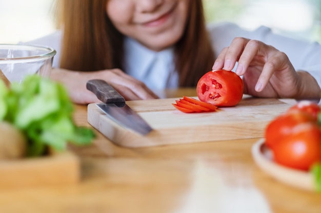 Close-up beeld van een vrouwelijke chef-kok die tomaat kijkt en snijdt met een mes op een houten bord