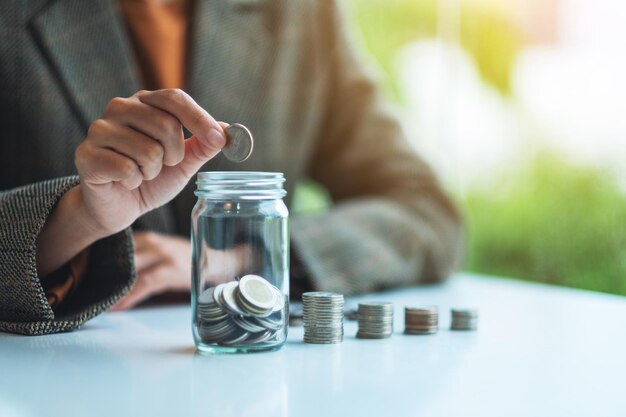 Close-up beeld van een zakenvrouw die munten verzamelt en in een glazen pot stopt om geld te besparen concept