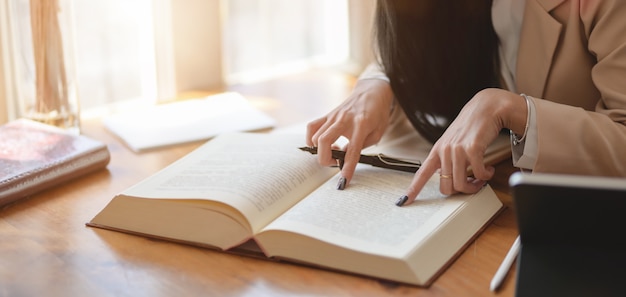 Close-up beeld van gepassioneerde zakenvrouw werken aan haar project tijdens het zoeken naar informatie uit de boeken