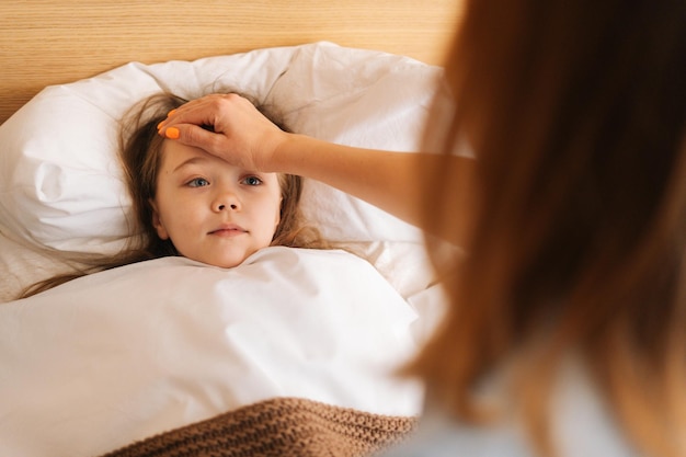 Close-up beeld van jonge moeder meet temperatuur raakt voorhoofd van zieke dochter die thuis in bed ligt