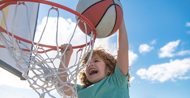 Close-up beeld van kind basketbalspeler die slam dunk maakt tijdens basketbalspel in schijnwerpermand
