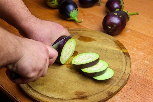Close-up beeld van mannelijke handen die aubergines snijden op een snijplank in de keuken