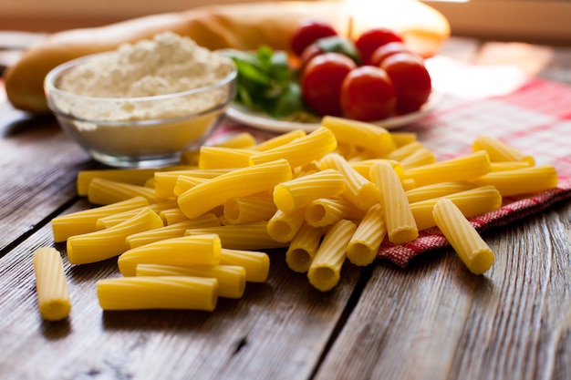 Close-up beeld van rauwe pasta en rode kerstomaatjes op de plaat kom tarwemeel op tafel