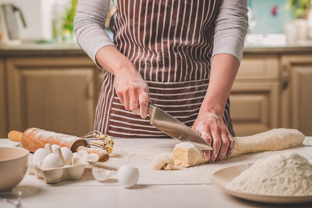 Close-up beeld van twee vrouwen handen gesneden mes deeg. Een vrouw in een gestreept schort kookt in de keuken