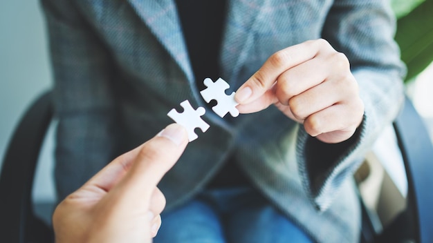 Close-up beeld van twee zakenvrouwen die een stukje witte puzzel bij elkaar houden en zetten