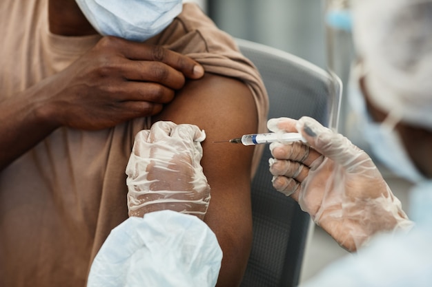 Close-up beeld van verpleegster in beschermende handschoenen die een vaccin tegen covid geeft aan patiënt in medic...