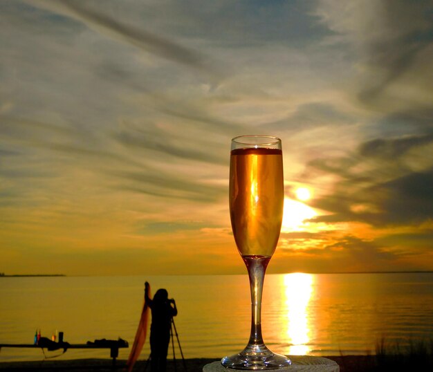 Close-up of beer glass on beach against sunset sky