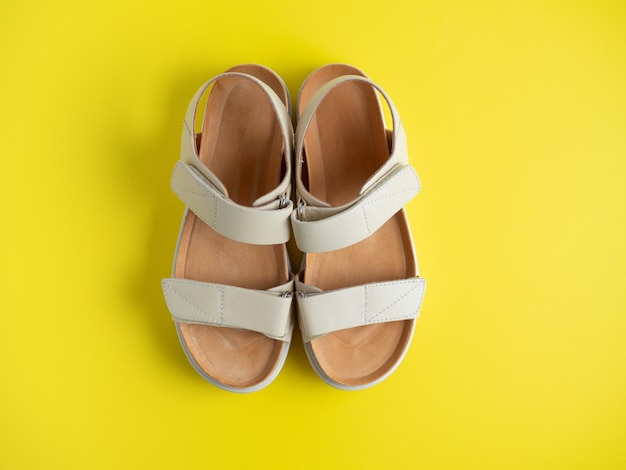 Close-up of beige leather sandals on a yellow background. A pair of shoes, women's flight shoes. Top view, flat lay