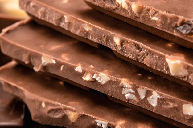 Close up of Belgian milk chocolate. Stack of milk and dark chocolate with nuts. Heap of chocolate bars. side view. Bitter chocolate on blurredbackground