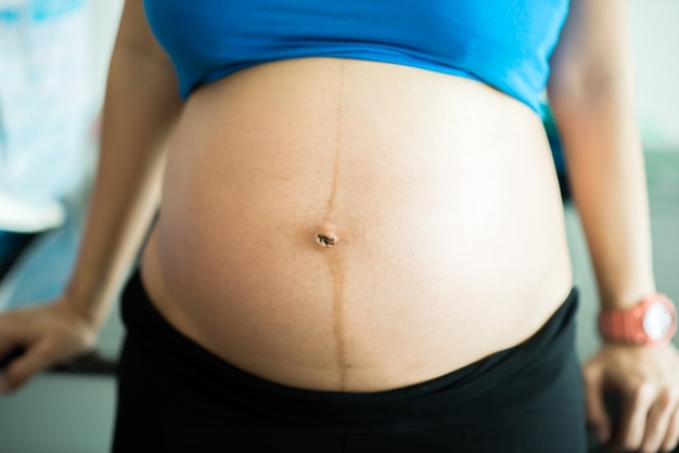 Close-up, belly and hands of the pregnant woman standing