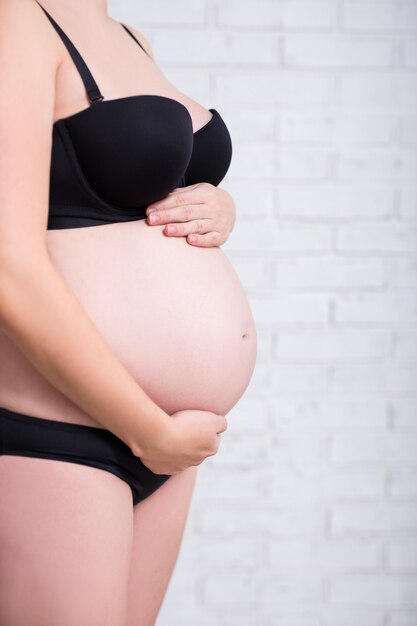 Close up of belly of pregnant woman over white brick wall