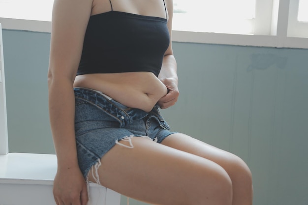 Photo close up of a belly with scar from csection and abdominal fat women's health a woman dressed up in sportswear demonstrating her imperfect body after a childbirth with nursery on the background