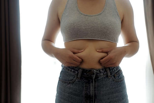 Photo close up of a belly with scar from csection and abdominal fat women's health a woman dressed up in sportswear demonstrating her imperfect body after a childbirth with nursery on the background