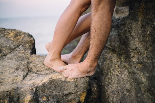 Close-up benen van kussend paar in de buurt van de zee op de rotsen
