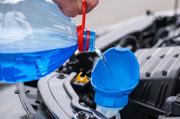 Close-up bestuurder die blauwe, niet-bevriezende ruitensproeiervloeistof in de tank van de auto giet