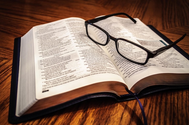 Photo close-up of bible and eyeglasses on table