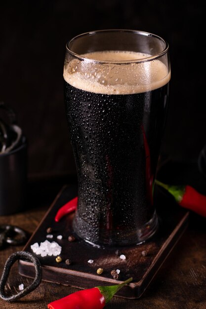 Foto close up di un grande bicchiere di birra scura fredda su uno sfondo nero con spuntini