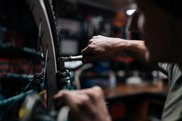Close-up bijgesneden opname van onherkenbare vakman die fiets repareert met behulp van speciaal gereedschap in fietsenmaker met donker interieur Concept van professionele reparatie en onderhoud van fiets