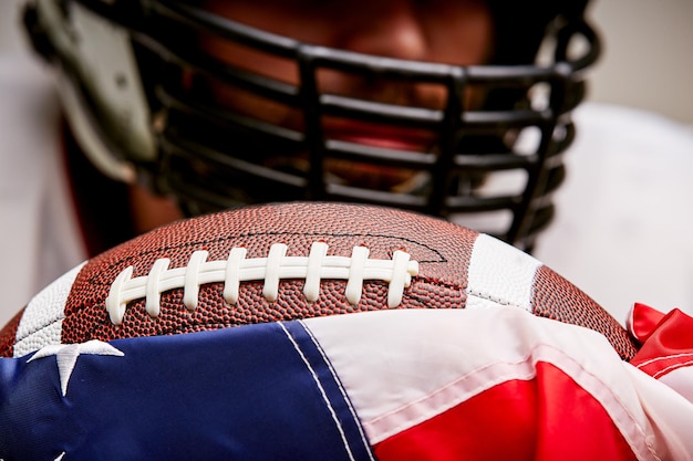 Close-up bijgesneden portret van voetballer in helm met bal en Amerikaanse vlag op een witte achtergrond