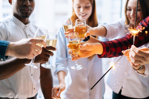 Foto close-up bijgesneden shot gelukkig business team van jonge multiraciale zakenmensen met bengaalse lichten en rammelende glazen champagne op bedrijfsfeest