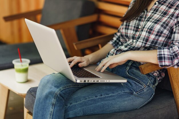 Close-up bijgesneden vrouw in buiten straat houten café zittend in casual kleding, werken op moderne laptop pc-computer, ontspannen tijdens vrije tijd. Mobiel kantoor