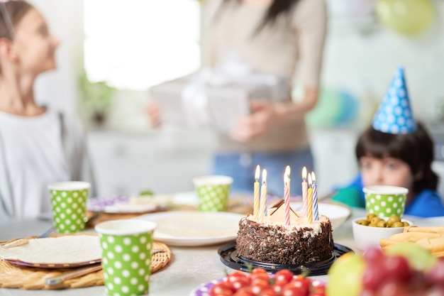 Primo piano di una torta di compleanno con candele sul tavolo. felice famiglia latinoamericana con bambini che festeggiano il compleanno a casa. messa a fuoco selettiva