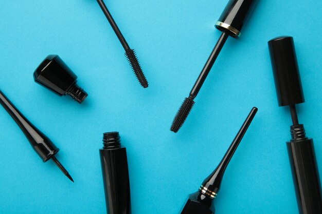 Close up of black eyeliners and mascara brush on blue background. Top view.