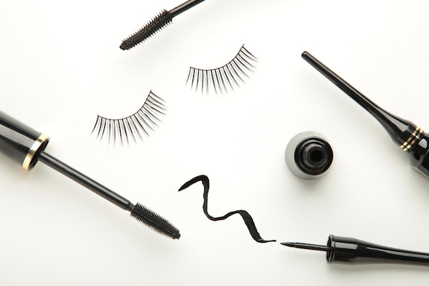 Close up of black eyeliners and mascara brush on white background. Top view.