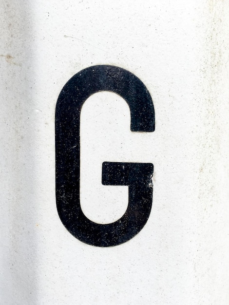 Foto close-up della lettera nera g sul muro bianco