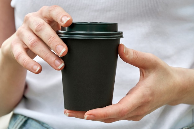 Close-up black paper cup with coffee in woman hands. Mock up