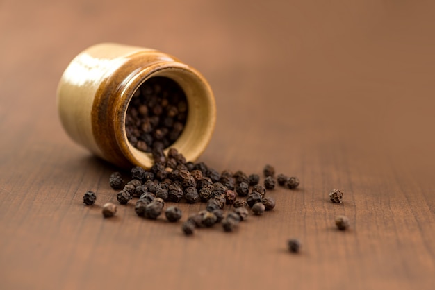 Close up of black pepper or peppercorns with clay pot